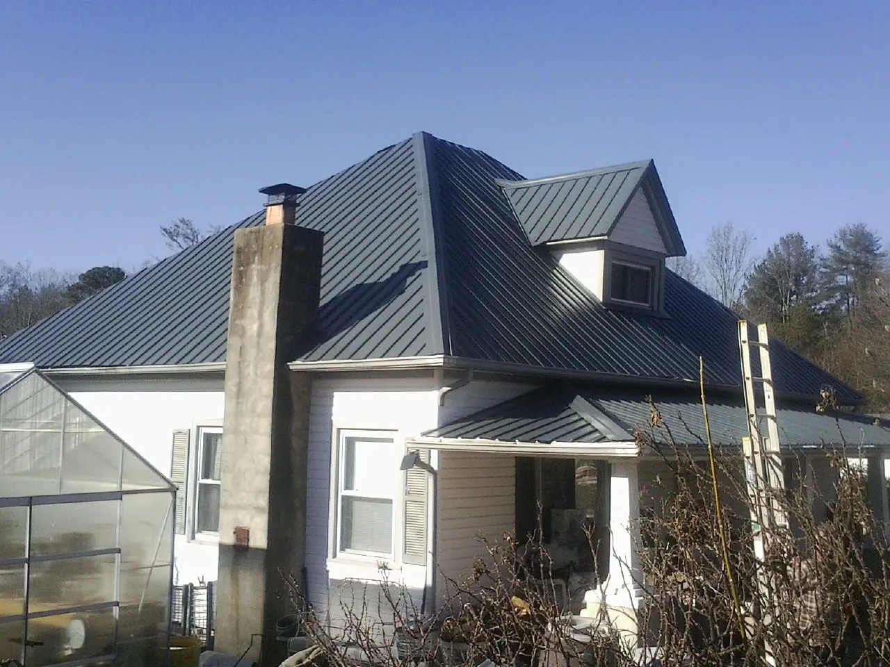 Dark blue standing seam metal roof on a white farmhouse with dormer — Slate & Tile Roof Repair by Roofing Brothers in North Henderson