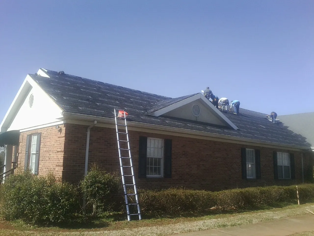 Crew tearing shingles off a brick ranch roof with a ladder set — Metal Roof Repair work by our crew in North Henderson