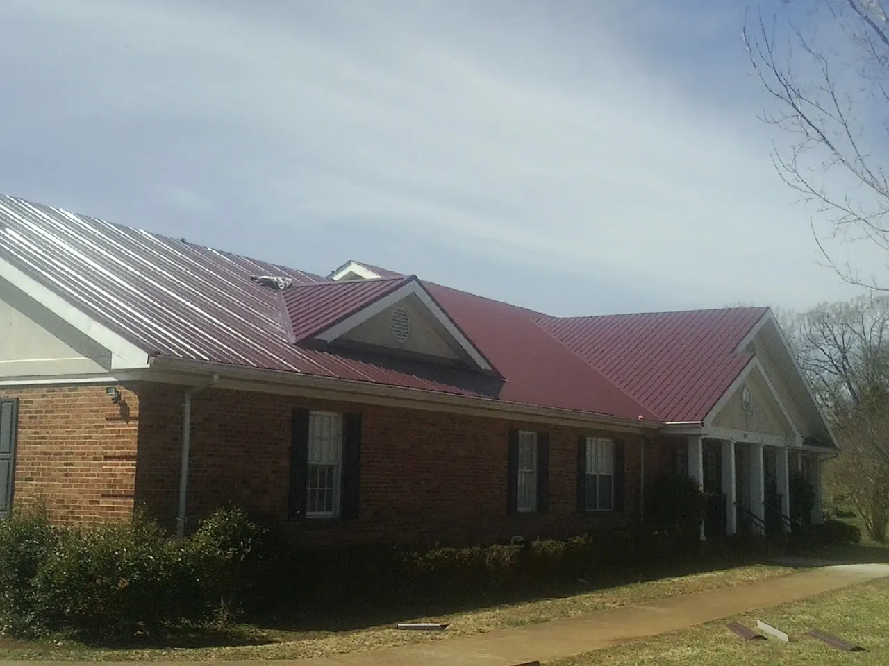 Red metal roof with gabled entries on a long brick building, from a Hail Damage Roof Repair job in North Henderson