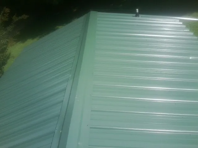 New green metal panels meeting at the ridge of a roof — Flat Roof Repair work by our crew in North Henderson