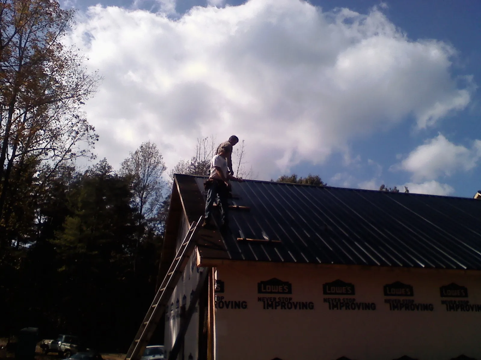 Roofer fastening dark metal panels high against a cloudy sky, from a Roof Inspection job in North Henderson