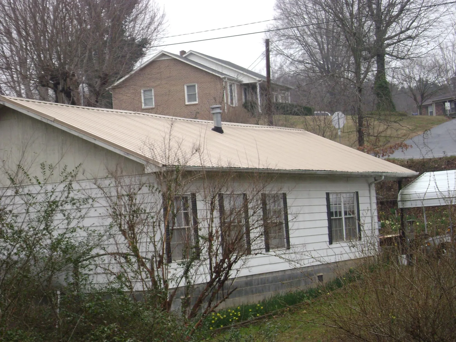 Tan metal roof on a white sided house set into a hillside — Commercial Roofing by Roofing Brothers in North Henderson