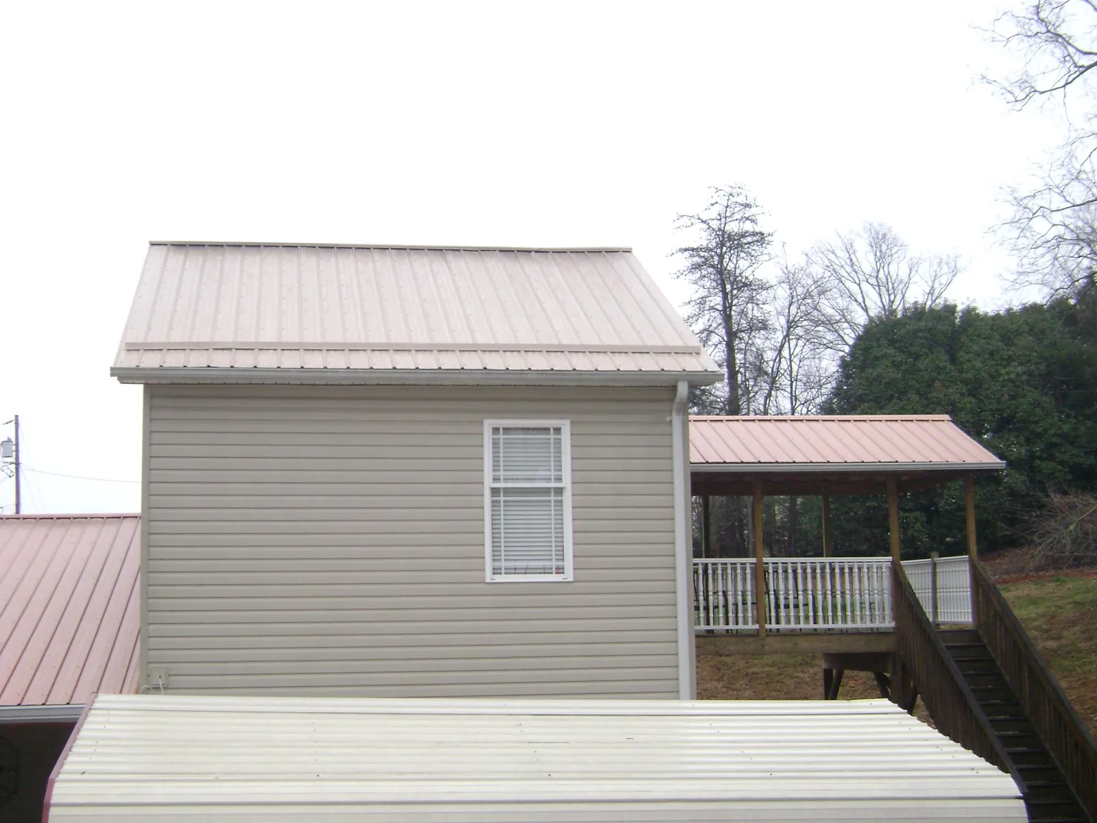 Tan metal roofs on a two story addition and attached porch, from a Roof Replacement job in North Henderson